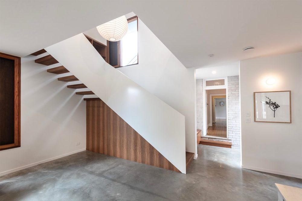 Floating timber staircase against a white wall over polished concrete
