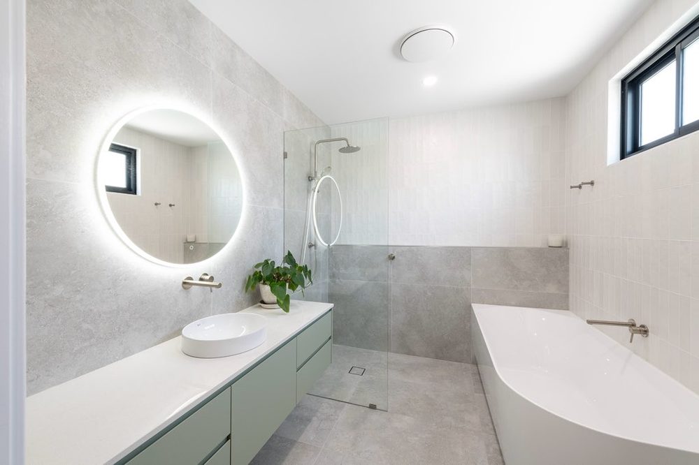 Bathroom with stone tiling, backlit round mirror and freestanding bath