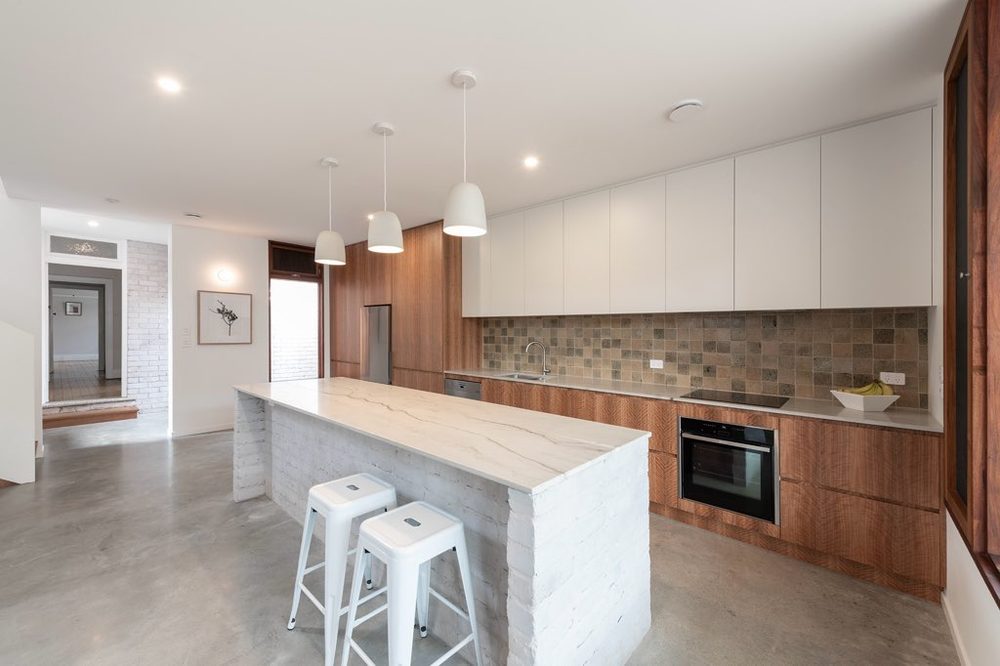 Open kitchen with island bench, white stools and timber cabinetry
